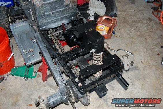Rear axle assembly of a lawn tractor, possibly undergoing repair or modification. Shows chains, springs, and suspension components