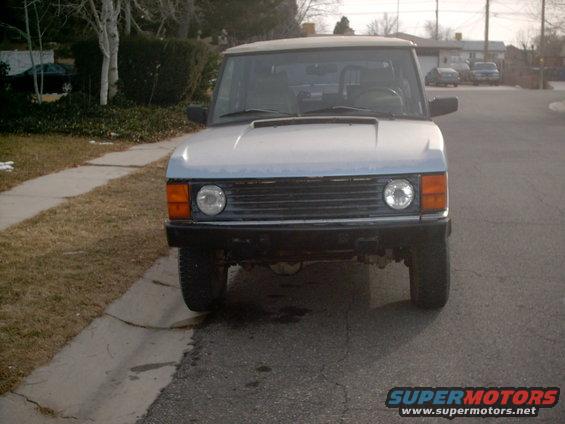 Light blue SUV parked on asphalt, front view. Round headlights, black grille, and orange turn signals are visible
