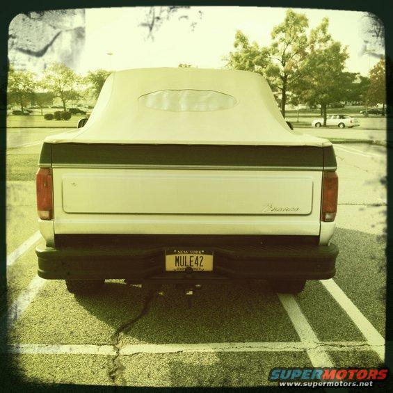 White Ford Bronco with a tan soft top parked in a lot, rear view