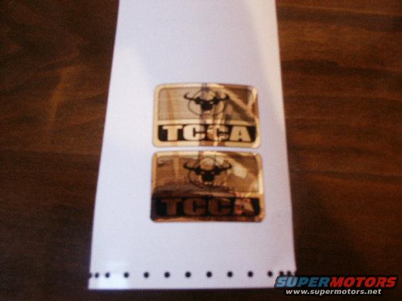 Two gold emblems with a bull logo and 'TCCA' text on a white sheet