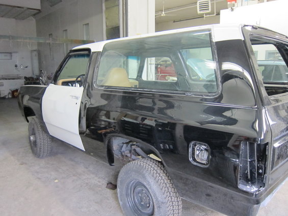 Black and white Dodge Ramcharger in a garage, undergoing repairs. The driver's side door is open