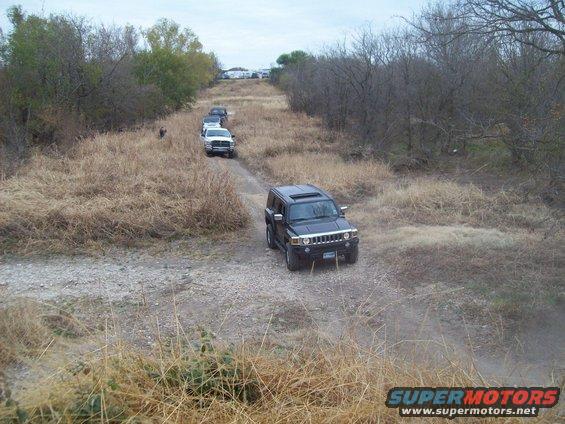 Black Hummer H3 on dirt road, three other SUVs behind