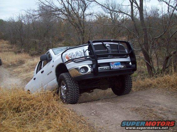 White pickup truck with a bull bar driving on a dirt path with dry grass and trees