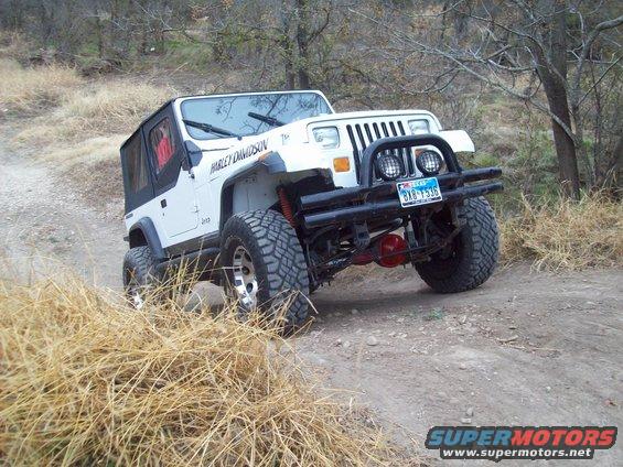 White Jeep Wrangler with black bumper and off-road tires on a dirt path