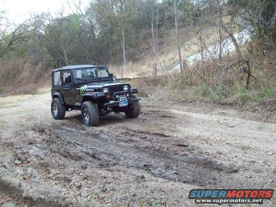 Black Jeep Wrangler with Monster Energy decals driving on a muddy trail