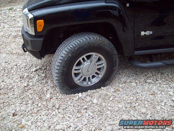Black SUV front fender and flat tire on gravel