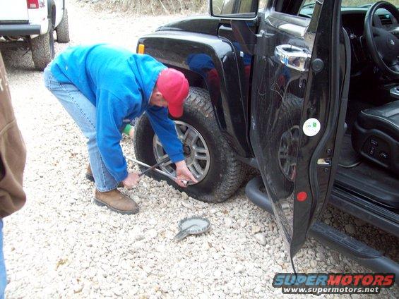 Black SUV with flat tire, man using a lug wrench