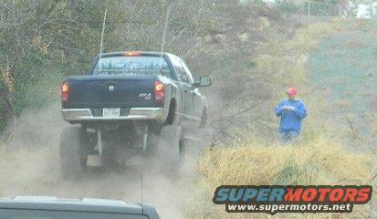 Black lifted pickup truck driving on a dirt road, kicking up dust