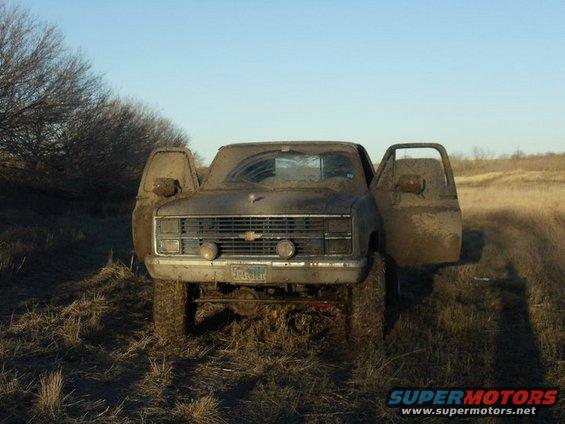 Front view of a muddy 1985 Chevrolet C/K pickup truck with doors open