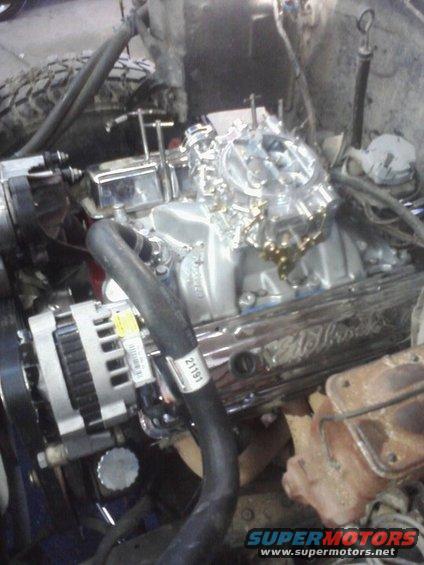 Close-up of a V8 engine with a Holley carburetor and a chrome Edelbrock valve cover. Alternator visible