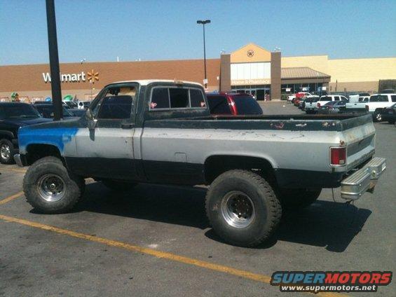 Two-tone pickup truck with blue painted front fender, lifted suspension, and large tires, parked in a lot