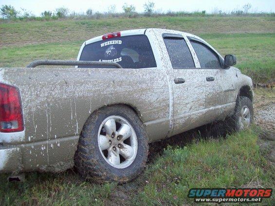 Mud-covered pickup truck stuck in grass with 'WEEKEND 4 WHEELERS' sticker on rear window
