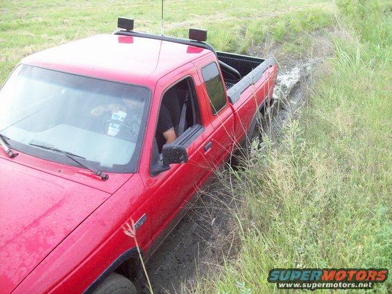 Red pickup truck with roof rack stuck in a muddy ditch off-road