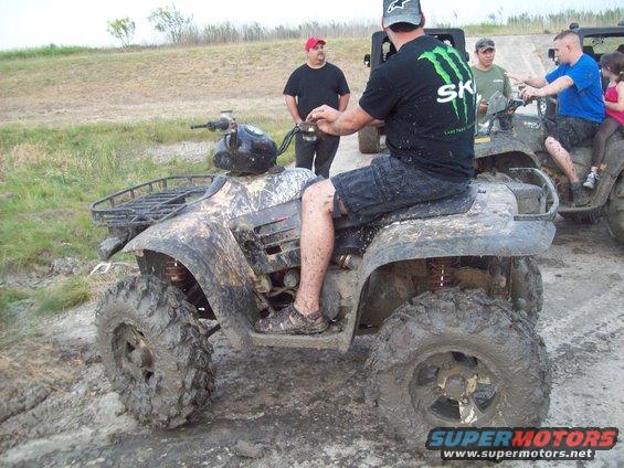 guy on a muddy ATV, another ATV behind him with people on it