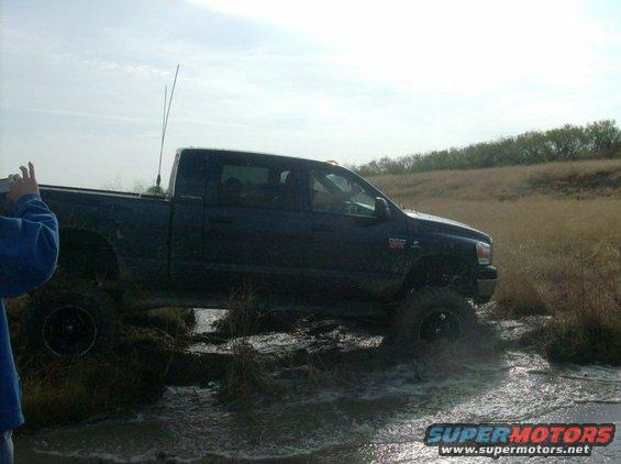Dark blue pickup truck with lifted suspension driving through muddy water
