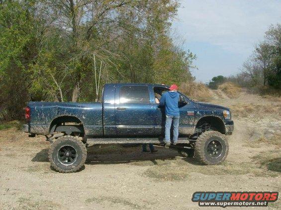 Blue lifted pickup truck with people getting in, off-road