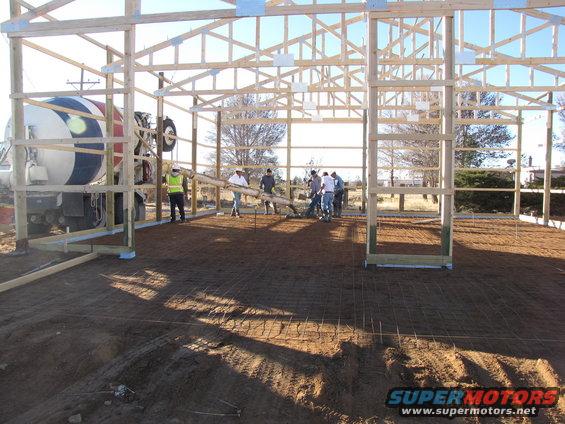 Construction site with a cement truck and workers pouring concrete inside a wooden frame building