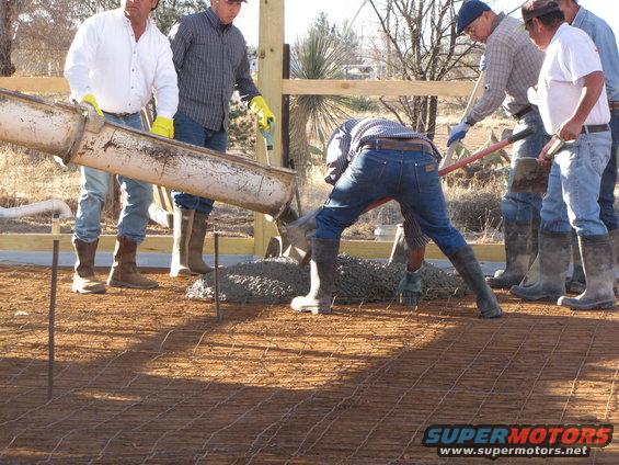 Workers pour concrete from a chute onto a rebar grid