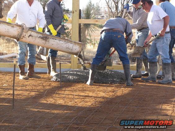Construction crew pouring concrete from a chute onto a rebar-reinforced ground