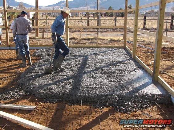 Workers pour concrete for a new building foundation. One man uses a shovel to spread the wet cement