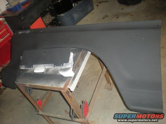 Vehicle fender, possibly primed, resting on a metal stand in a workshop