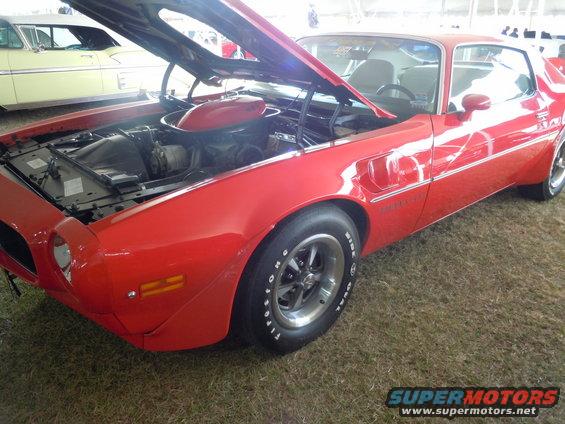 red coupe with hood open, showing engine. another car in background