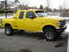 1996 Ford F-150 - This yellow Ford F-150 pickup truck features a distinctive bed cap and lifted suspension, seen in a suburban setting.