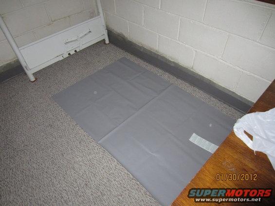 Gray floor mat on carpet next to a white metal rack and wooden surface. Date stamp 01/30/2012