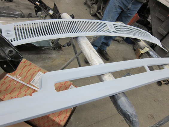 Car grille and trim pieces, one with vertical slats, resting on sawhorses. Box with 'VAIP' visible