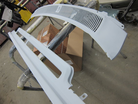 Two unpainted vehicle body parts, possibly a grille and a trim piece, resting on stands in a workshop
