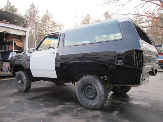 Black and white SUV in disrepair, side view. Missing rear bumper and taillights