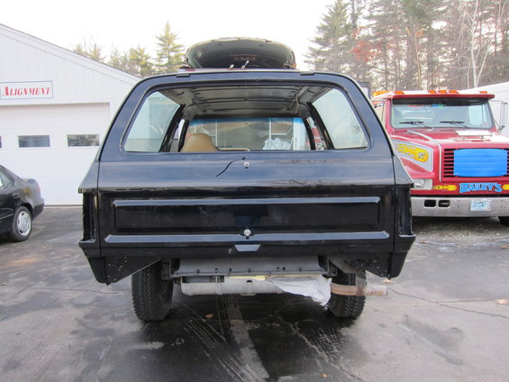 Black SUV, rear view, spare tire on roof. Red tow truck in background