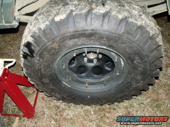 Close-up of a large off-road tire and black wheel, supported by red jack stands