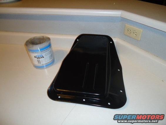 Black metal pan with bolt holes and a roll of Speed Seal sealant on a white countertop