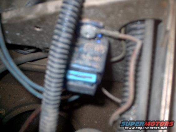 Close-up of a blue connector on a vehicle part, with hoses and wires visible