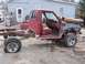 1987 Ford Ranger - A red pickup truck chassis sits in a yard, missing its front end and with a flat tire.