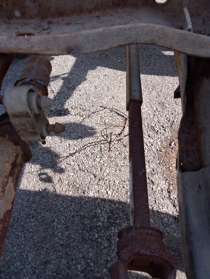rusted metal frame parts and a driveshaft under a vehicle