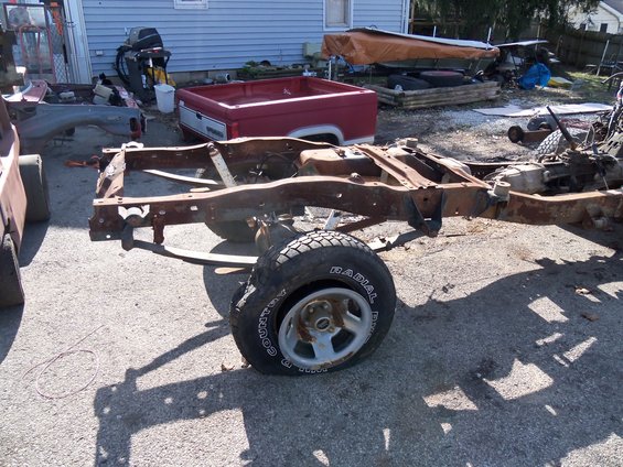 Rusted truck frame and red bed, front wheel visible