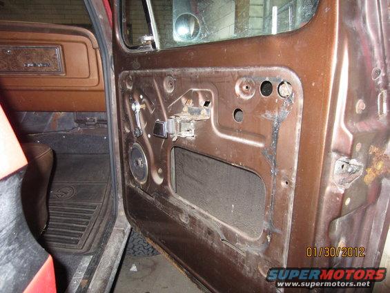 Brown interior door panel of a 1979 Ford Bronco with exposed metal and window crank