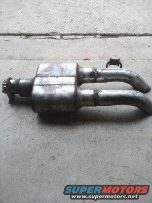 Dual exhaust system with a central muffler and two curved pipes, resting on a concrete surface