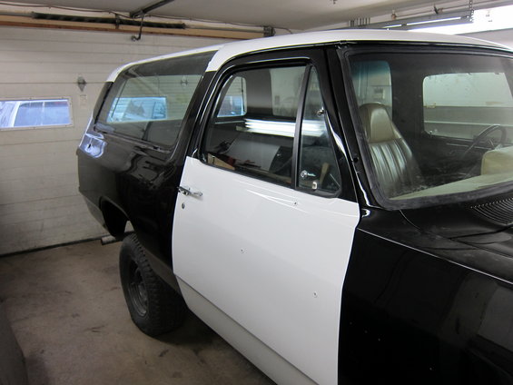 Black and white SUV, looks like it's being worked on in a garage. Side door is white, rest of the body is black