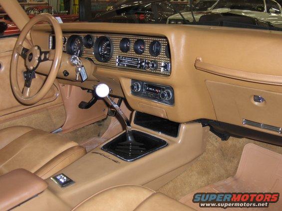 tan interior of a 1977 Pontiac Firebird, showing steering wheel, dashboard gauges, and center console with shifter