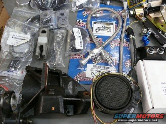 Assortment of car parts including a black bracket, braided hose, speaker, and various hardware pieces