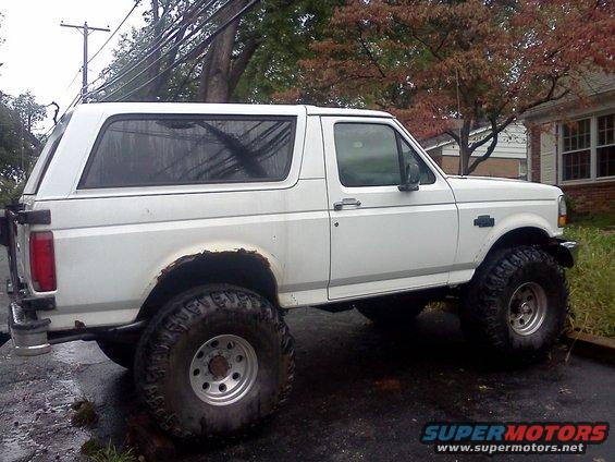 White 1996 Ford Bronco with lifted suspension and oversized tires, seen from the side