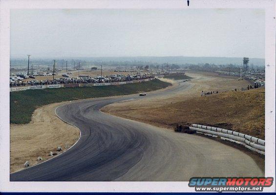 Race track scene with cars and spectators, one car on track