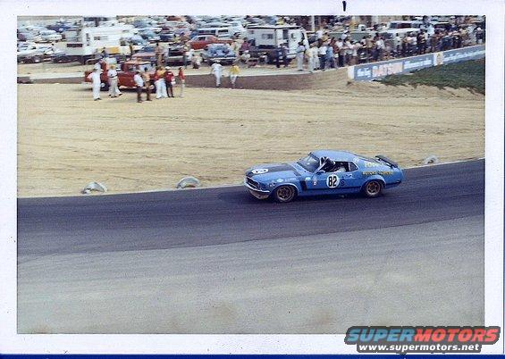blue race car with number 82 on track, spectators in background