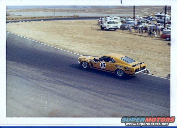 Yellow 1970 Ford Mustang Boss 302 race car with number 16 on door, driving on a track