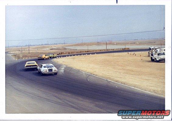 White race car with black stripes on a track, viewed from rear