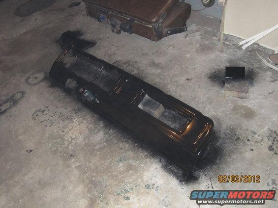 Black dashboard assembly on concrete floor, spray paint can nearby