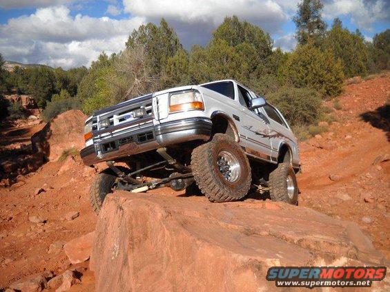 White Ford Bronco climbing a rock on a dirt trail